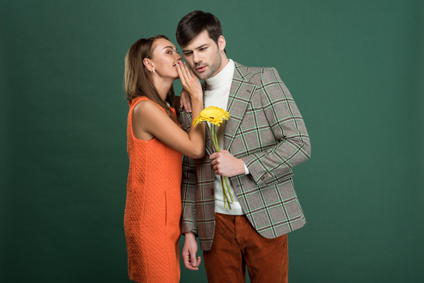 beautiful woman in vintage clothes whispering something to boyfriend with flowers isolated on green - Foto, Bild