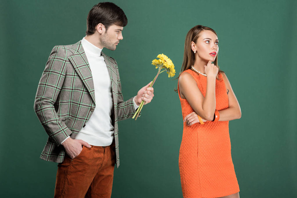 handsome man in vintage clothes presenting flowers to thoughtful woman isolated on green - Foto, Bild