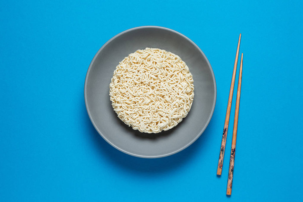 Fast instant noodles in grey bowl with chopsticks on a blue background with a place for copy space - Fotoğraf, Görsel