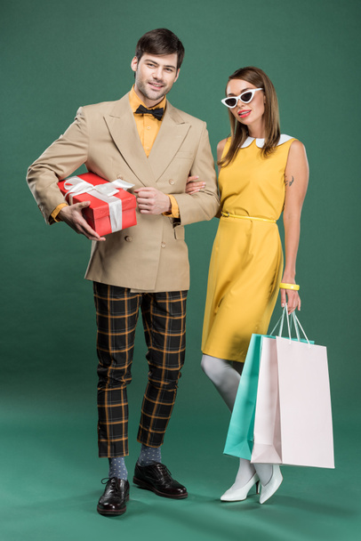 hermosa pareja en ropa vintage con bolsas de compras y caja de regalo sobre fondo verde
 - Foto, imagen
