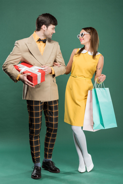 beautiful smiling couple in vintage clothes with shopping bags and gift box on green background - Photo, Image