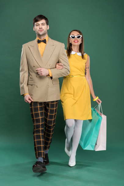 beautiful couple in vintage clothes with shopping bags on green background - Photo, Image