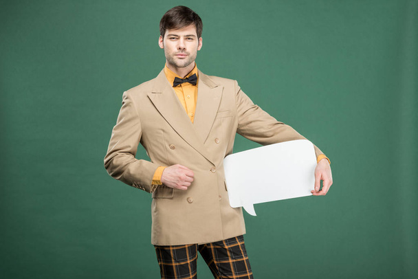 handsome man in vintage clothes holding speech bubble and looking at camera isolated on green - Foto, afbeelding