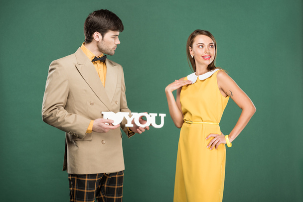 man presenting decorative 'i love you' sign to beautiful woman in vintage clothes isolated on green  - Photo, Image