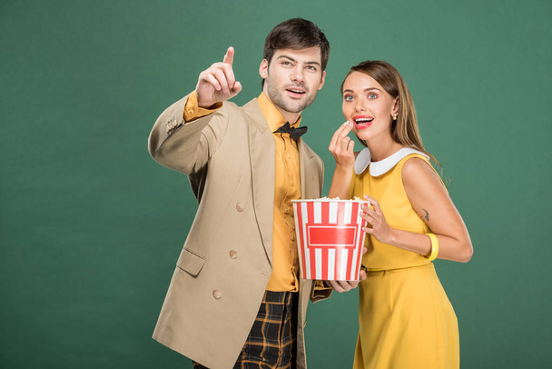 beautiful smiling couple in vintage clothes eating popcorn while watching movie isolated on green - Foto, Imagen