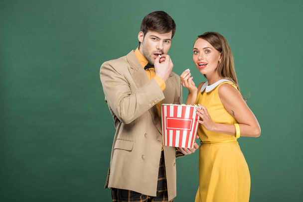 beautiful couple in vintage clothes eating popcorn while watching movie isolated on green - Foto, Imagem