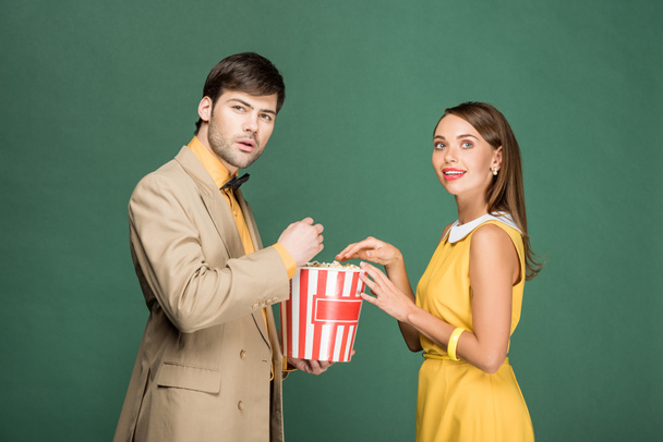 beautiful couple in vintage clothes watching movie with popcorn isolated on green - Photo, Image