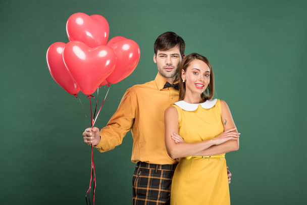 beautiful couple with heart shaped balloons looking at camera isolated on green - Fotoğraf, Görsel