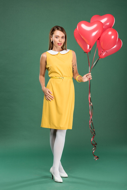 beautiful woman holding heart shaped balloons and looking at camera on green background - Photo, image