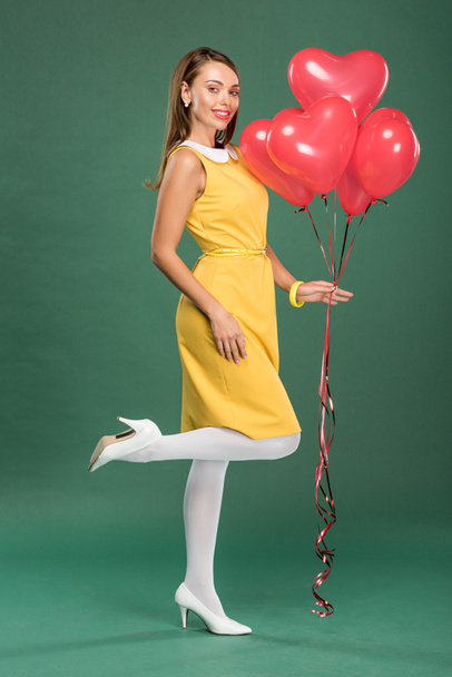 beautiful woman holding heart shaped balloons and looking at camera on green background - Foto, Imagen