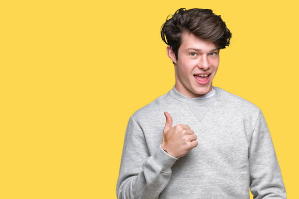 Young handsome sporty man wearing sweatshirt over isolated background doing happy thumbs up gesture with hand. Approving expression looking at the camera showing success. - Photo, Image