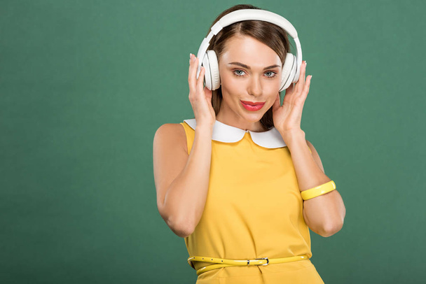 beautiful stylish woman in yellow dress and headphones looking at camera isolated on green - Photo, Image