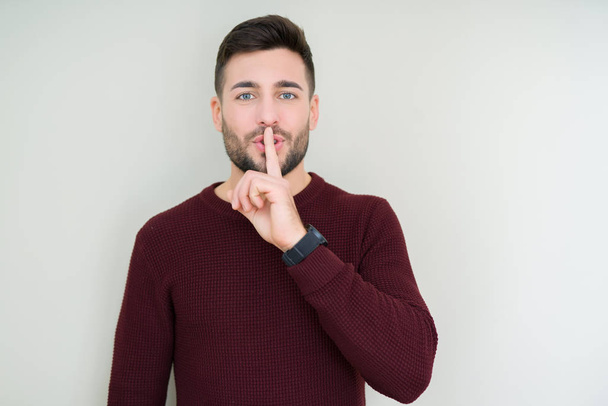 Jonge knappe man dragen een trui over geïsoleerde achtergrond vragen stil met de vinger op de lippen te zijn. Stilte en geheime concept. - Foto, afbeelding