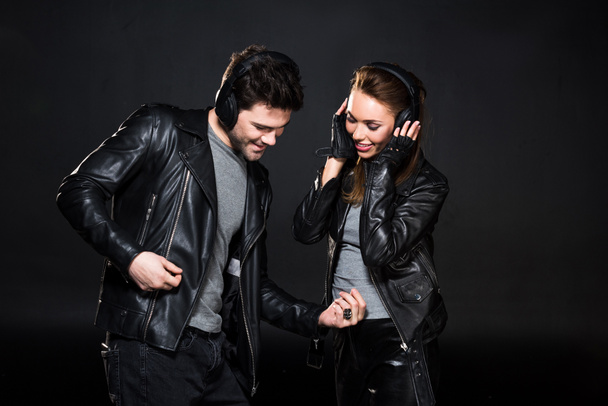 hermosa pareja en auriculares y chaquetas de cuero escuchando música aislada en negro
 - Foto, Imagen