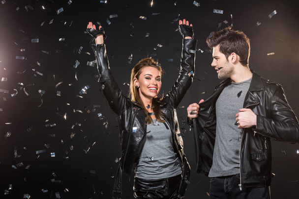beautiful couple in leather jackets cheering with falling confetti on black background - 写真・画像