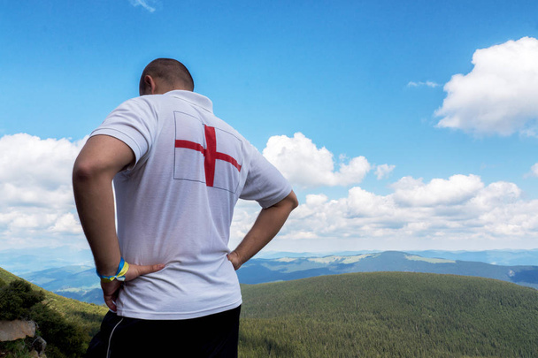 Turista in camicia bianca con una croce rossa che ammira il paesaggio
 - Foto, immagini