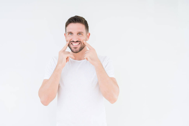Mladý pohledný muž nosí ležérní bílé tričko přes izolované pozadí s úsměvem s otevřenými ústy, prsty směřující a nutí veselým úsměvem - Fotografie, Obrázek