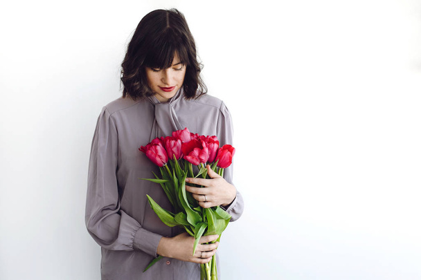 Beautiful brunette girl holding stylish bouquet of tulips on white background indoors, space for text. Happy young woman with flowers. Happy mothers day. International womens day - Photo, Image