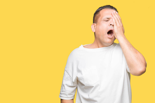 Арабський чоловік середнього віку носить білу футболку на ізольованому фоні, втомлюючись покриваючи половину обличчя, очі і рот рукою. Болить обличчя від болю
. - Фото, зображення