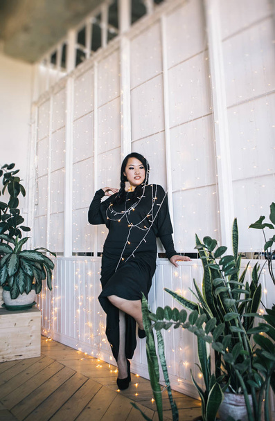 Korean woman in black dress posing wrapped in garland with one lifted leg - Foto, Imagem