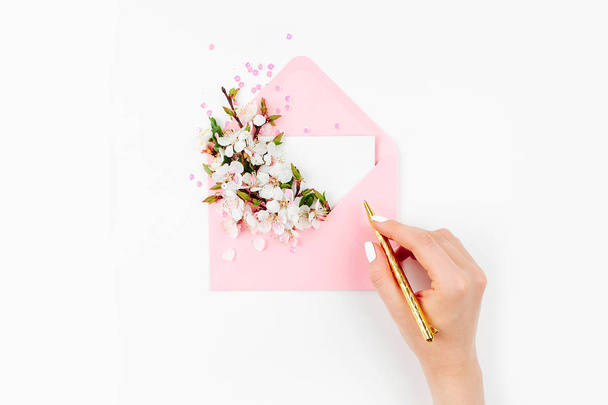 Vrouwelijke hand en roze envelop met een lente-bloemstuk. Plat lag, top uitzicht. - Foto, afbeelding