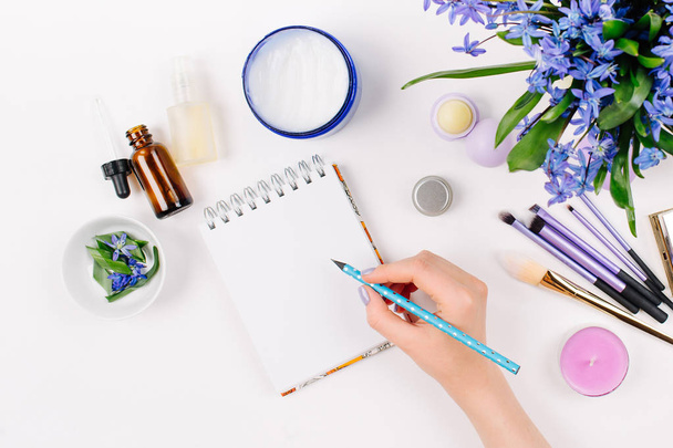 A woman writes in a notebook. Background with Blue spring bouquet, homemade cosmetics and accessories. Styled flat lay mockup. Copy space - Fotó, kép