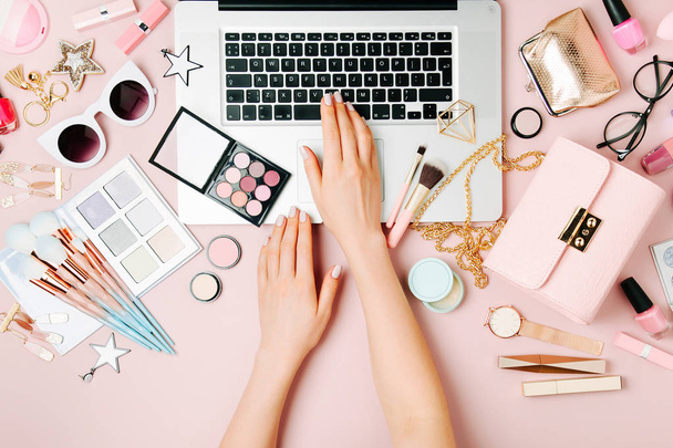 Fashion blogger working with laptop. Workspace with  female accessory, cosmetics products on pale pink table. flat lay, top view - Foto, immagini