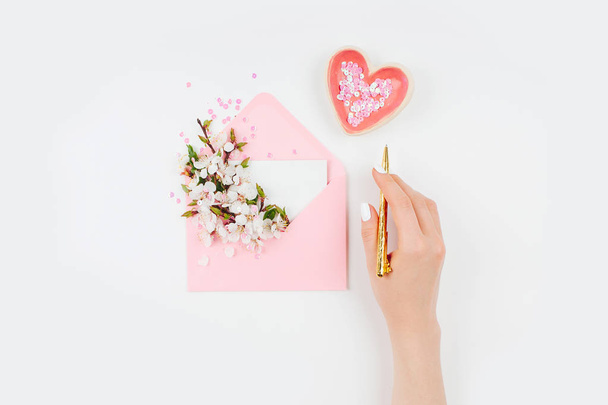 Female hand and Pink envelope with a spring flower arrangement. Flat lay, top view. - Foto, afbeelding