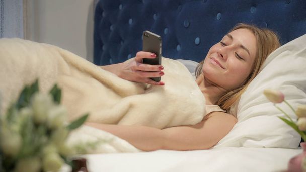 Blondynka, leżąc w łóżku pisania wiadomości na Twój telefon - Zdjęcie, obraz