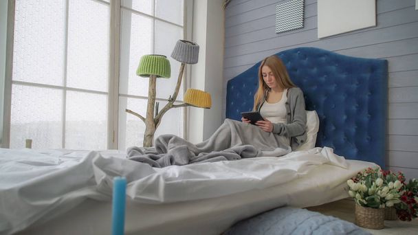 Nuori tyttö istuu sängyssä tabletin kanssa
 - Valokuva, kuva