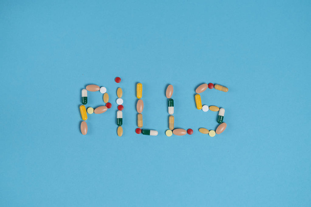 word pills is laid out from colorful pills on a blue background with a place for copy space - Fotó, kép
