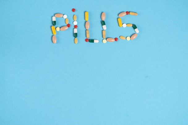 woord pillen van kleurrijke pillen op een blauwe achtergrond met een plek voor kopie ruimte is aangelegd - Foto, afbeelding