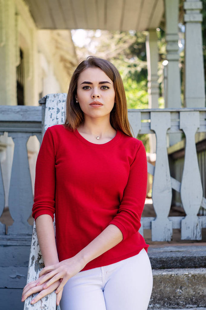 Portret van een meisje. gekleed in een rode jas. Op de trap rond het huis. - Foto, afbeelding