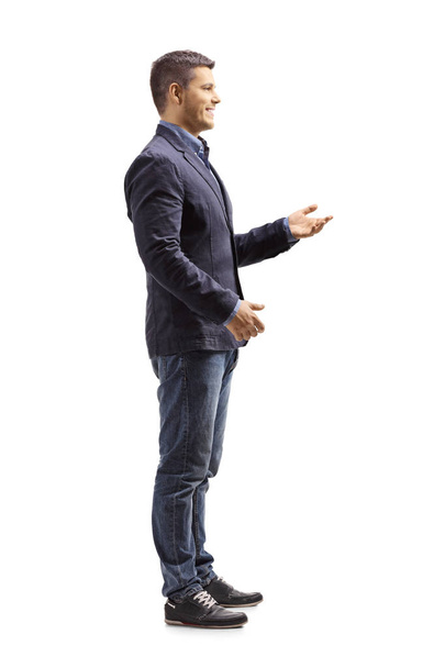 Full length profile shot of a young man standing and gesticulating a conversation isolated on white background - Foto, Imagen