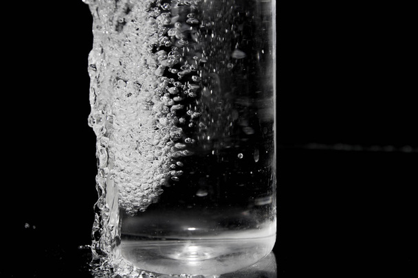 Splash water op zwart, stijlvol plons water. Geïsoleerd op zwarte achtergrond, bubbels in het glas, de mist op het glas, water gegoten in het vaartuig - Foto, afbeelding