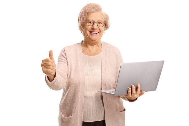 Happy senior woman holding a laptop computer and showing thumbs up isolated on white background - Photo, image