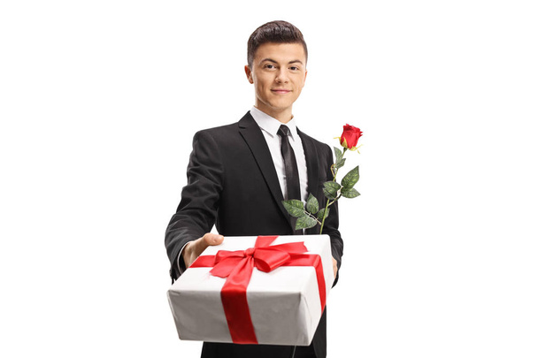 Handsome young man in a suit giving a present and a red rose isolated on white background - Fotoğraf, Görsel