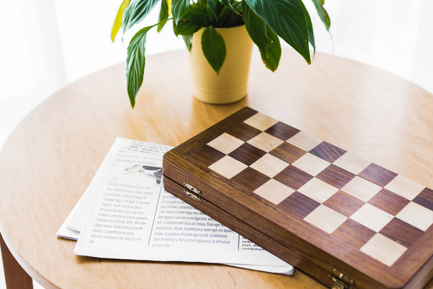 wooden chess board near newspaper and plant on coffee table  - Zdjęcie, obraz