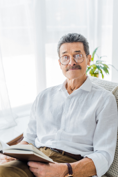 retired man in glasses holding book and smiling at home - Foto, Imagem