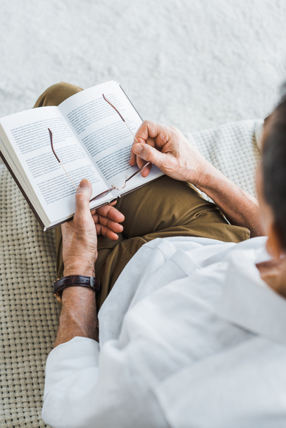 selective focus of senior man holding book and glasses at home - Photo, Image