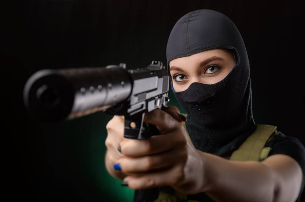ヘイズの暗い背景の上に手で銃を持つポーズ軍の特別な服の女の子 - 写真・画像