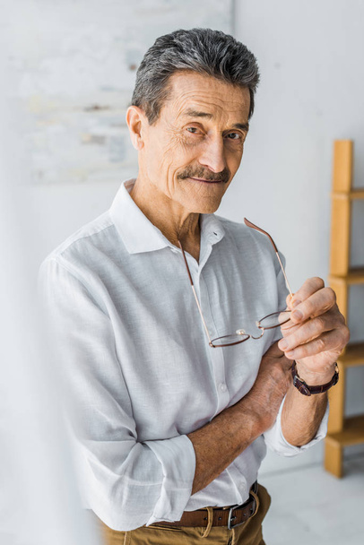 happy senior man holding glasses and smiling at home - Photo, Image