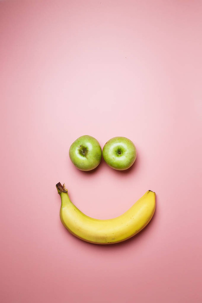 Smiley face with two apples and a banana with copy space on a pink background - Photo, Image