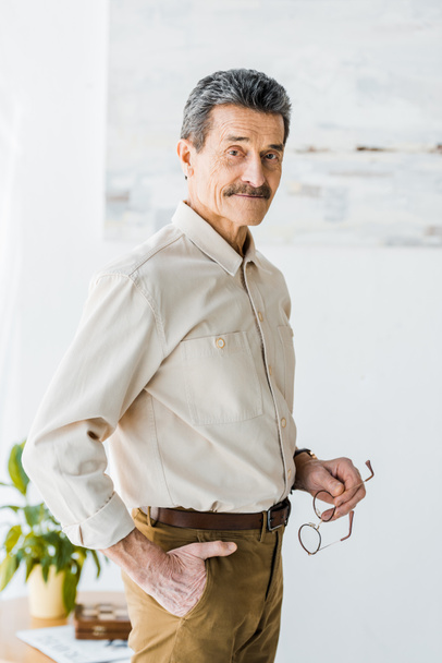  senior man standing with hand in pocket and holding glasses - Photo, Image