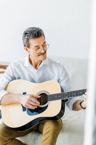 cheerful senior man in glasses playing acoustic guitar at home - Photo, Image
