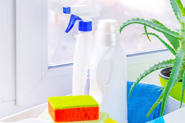 Spring cleaning at home. Window cleaning using bottle cleaners. The concept of cleanliness and comfort. Against the background of the window detergents, cleansers and aloe. Outside the city, blurry - Photo, Image