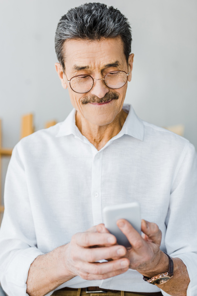 hombre mayor alegre en gafas mirando el teléfono inteligente en casa
 - Foto, Imagen