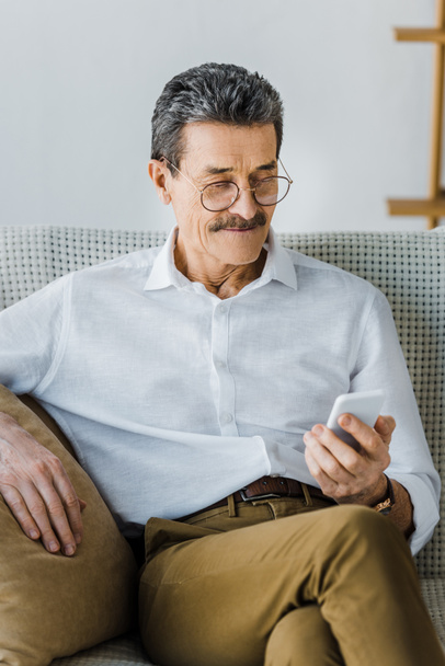hombre mayor feliz en gafas mirando el teléfono inteligente en casa
 - Foto, Imagen