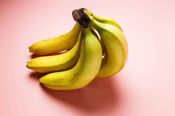 ピンクの背景のエクアドル産バナナの 5 個の束。バナナは、少し傷と少し緑が非常においしい. - 写真・画像