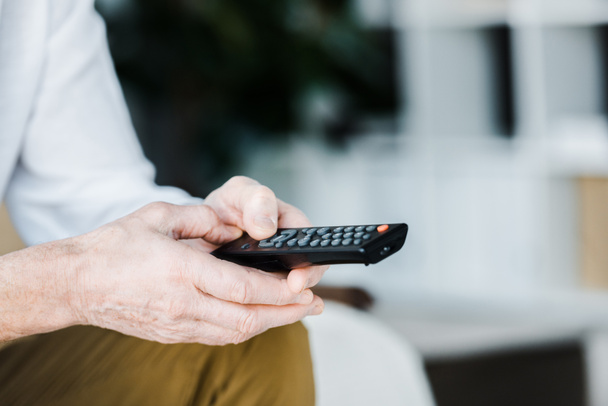 cropped view of senior man holding remote control in hands - Foto, Imagem